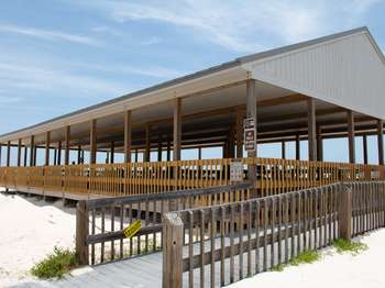 A wooden structure on white sand with a wooden ramp in front and a bright blue sky in the background.