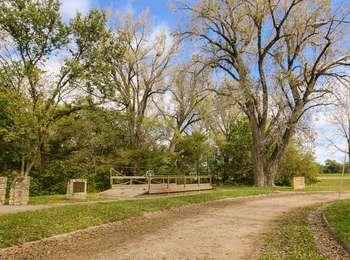 Dirt round lined with grass meadows and trees passing by a wood, replica rope ferry