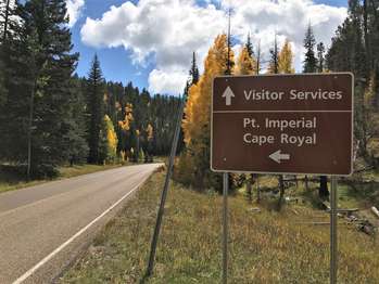 A brown rectangular sign with white lettering mounted on two metal posts reads at the top,