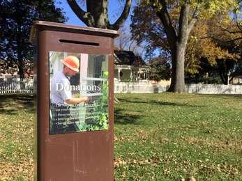 A brown donation box has a slot for deposits and a sign explaining how the money is used.