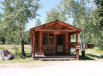 Small log cabin serving as office for the Murie Ranch of Teton Science Schools. Brochure box for self-guided tour to the right of the office and a boulder with a plaque designating the ranch as a National Historic Landmark to the left.