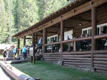 People climb stairs onto the wide porch of a rustic log building
