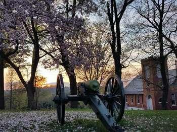a landscape at sunset with flowering trees, an artillery piece, and a brick church