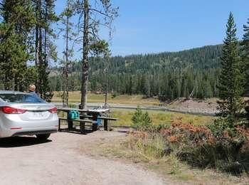 Silver car and visitor setting up for a picnic at the Flagg Canyon picnic area. Snake River is beyond with someone fishing.