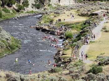 Crowds of people walk on a trail to a river crowded with swimmers