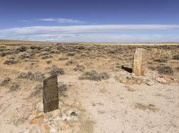 An endless plain covered in sagebrush and dried grass with two, inscribed, vertical stone markers in the foreground