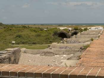 View of a series of exposed brick arches going vertically down the center of the image. The Gulf of Mexico and blue sky in the background.