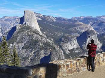 A person takes a photo of the scenery, which includes Half Dome and surrounding rock formations, on his cell phone.