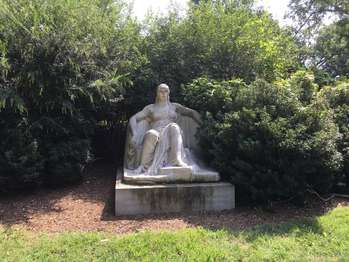 A stone statue of a woman with a gown on, sitting in a chair