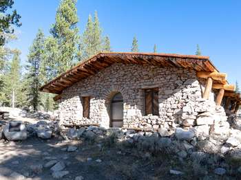 A stone building with a wooden roof stands on a small hilltop.