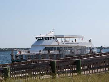 Two deck white boat in water next to a wooden dock structure.