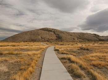 Pathway leading through grass and sagebrush plains to a larger dome shaped natural rock formation