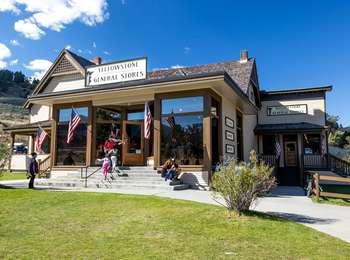 People approach an entrance of a wood building with large windows and US flags behind a lawn