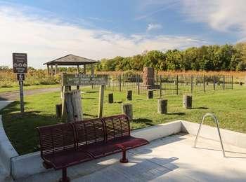 A moderately developed park with benches, a monument and a gazebo set in a landscape of prairie and forest