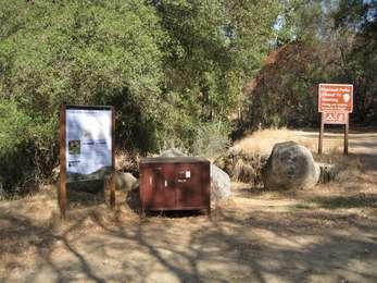 Trailhead placard, closed to a no hunting sign and bear box in front of oak trees