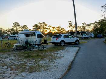 A white truck pulls a silver camper onto a black asphalt road. Trees in the background.