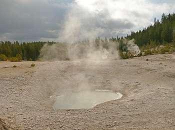 A small, muddy pool with steam rising surrounded by dry mud