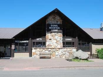 Front of Signal Mountain Lodge building that houses gift shops and restaurants. Stone facade in center with tan building and dark brown trim.