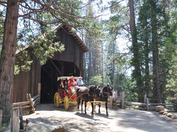 A bright red horse-drawn stage exits an old covered wooden bridge.