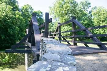 Landscape shot of bridge going over the Shenandoah Canal. The bridge is supported by stone pillars and has wooden sides. It leads to the Virginius Island trail on one side and on the other leads to Shenandoah Street. 