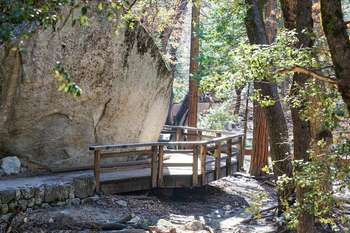 A wooden path with a wood railing circles around a large granite boulder.