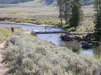 Hikers on the trail as it approaches a bridge crossing a river.