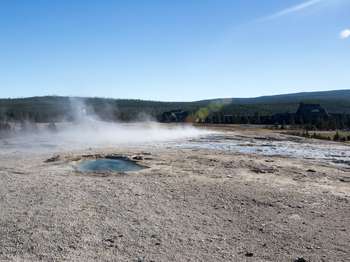 Steam rises from a barren landscape where the opening to Giantess Geyser is hidden from view.