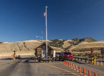 A US flag flies above a small log cabin with traffic lanes on either side and cars