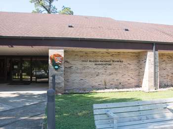 A light brown brick building with a dark brown roof. The National Park Service orange and green arrowhead logo on the building. Black text reads, 