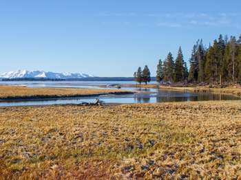A creek meanders across a wetland as it heads toward a large lake and mountain.