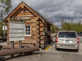A person in a minivan receives papers from a ranger leaning out of a small cabin with a sign of entrance fees