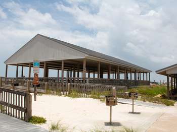 Wooden pavilion structure on a white sand beach with wooden picnic tables underneath.