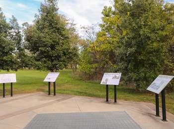 Interpretive wayside signs on metal poles with grass and trees in the background