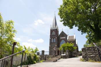 Very tall, stone church with stained glass windows and white crosses. Trees and Loudoun Heights are around it.
