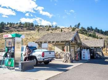A man pumping gas into a truck at a single gas pump at a small log and stone building with ice machine