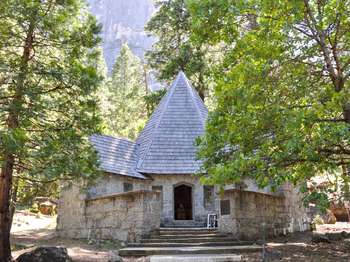 A stone building is surrounded by oak, cedar, and pine trees.