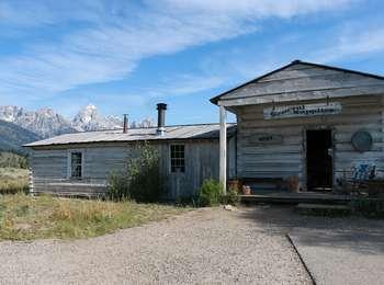 Front of Menors cabin and general store that are whitewashed. The Teton Range dominates the skyline above the cabin.
