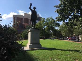 A statue of Edmund Burke with his right hand in the air on top of pedestal