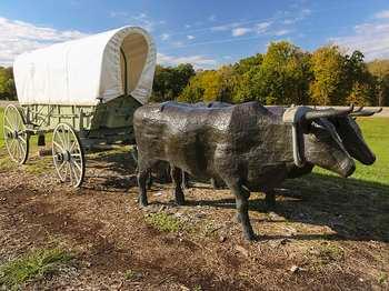 Life-size sculpture consisting of two, metal oxen hooked to a replica, covered wagon