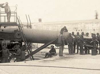 Black and white photo of soldiers loading a rifle on top of Battery Pensacola.