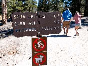 Two people walk past a metal sign that lists the hiking destinations of the trail they're on.
