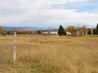 White Oregon Trail marker stands in a dry grass meadow, with a rural city park and a lake in the background