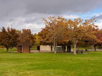 Grass lawn in foreground gives way to trees in fall color, concrete sidewalks, picnic tables, and several small structures