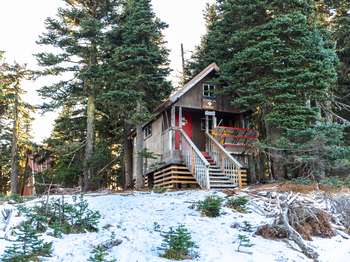 A small hut in the snow on stilts, with stairs leading to the front door.