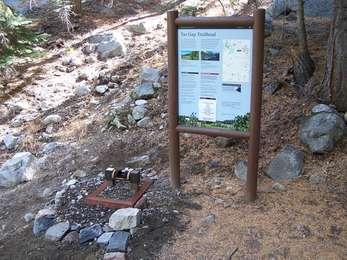 A trailhead sign and a boot brush installed nearby