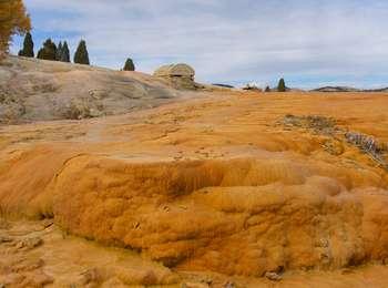 Orange and yellow colored rock surrounds a small, steaming geyser