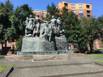 A statue of two groups of men shaking hands, one man sits between them. 