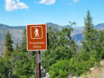 A brown and white road-side sign reads Poopenaut Valley and has an hiker icon. Trees and a steep valley can be seen in the distance.