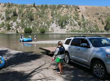Visitors getting ready to launch a blue raft on the Snake River with a white SUV and a trailer.