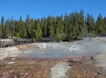 Steam rises from a blue pool with red edges and orange streamers next to a boardwalk